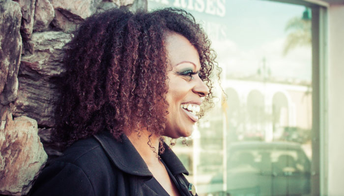 woman with dark curly hair leaning against stone wall and smiling