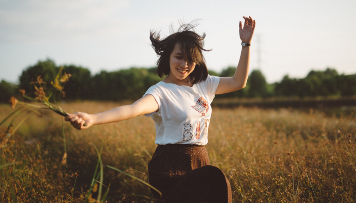 Brunette woman wearing a brown skirt smiles while prancing and holding wildflowers in a golden field