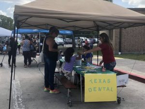 The Texas Dental outdoor table under a large umbrella at the Spring Meadows Elementary Back-to-School Block Party