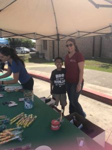 Jenna, the office manager at Texas Dental, smiles with an elementary school student by a table of toothbrushes
