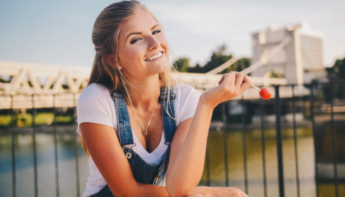 blond girl in coveralls smiling holding a lollipop